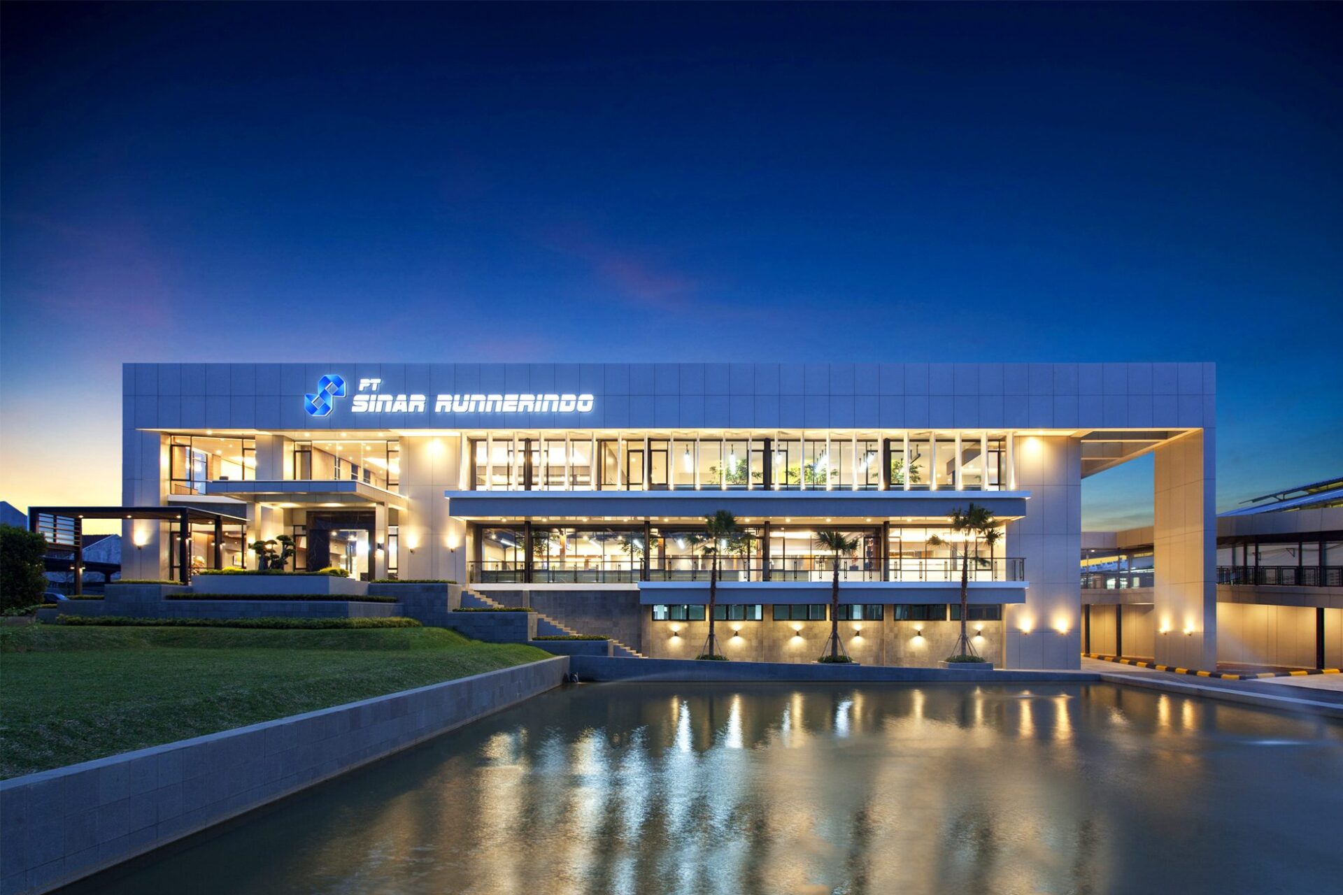 The PT Sinar Runnerindo building with its illuminated sign at dusk, behind a reflecting pool