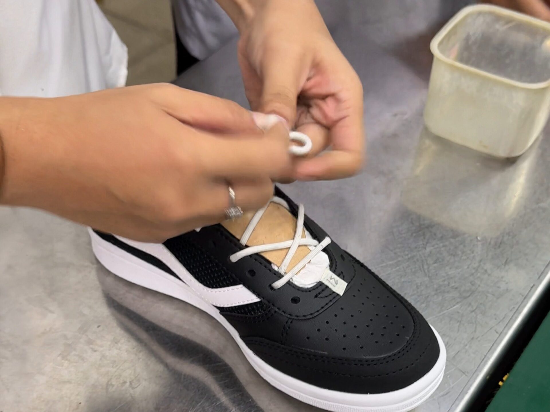 Tangan operator memasang tali pada sepatu jadi di meja finishing